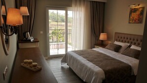 A hotel room with a large bed, two bedside tables with lamps, a wooden desk with a tray of items, and a balcony with a view of greenery. - Sarban Hotel (Fethiye)