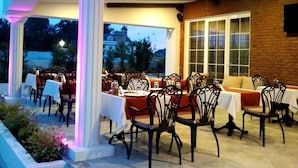 An outdoor dining area with tables and chairs, a brick wall, and a large window. - Sarban Hotel (Fethiye)