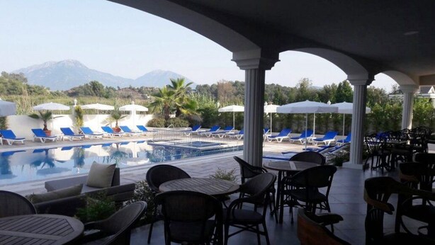 A poolside area with lounge chairs and tables, a pool, and a view of mountains. - Sarban Hotel (Fethiye)