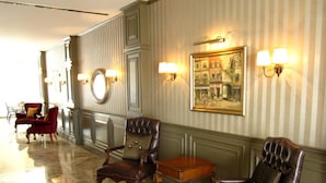 A hotel lobby with a marble floor, leather armchairs, a small wooden table, and wall-mounted lamps. - Sarban Hotel (Fethiye)