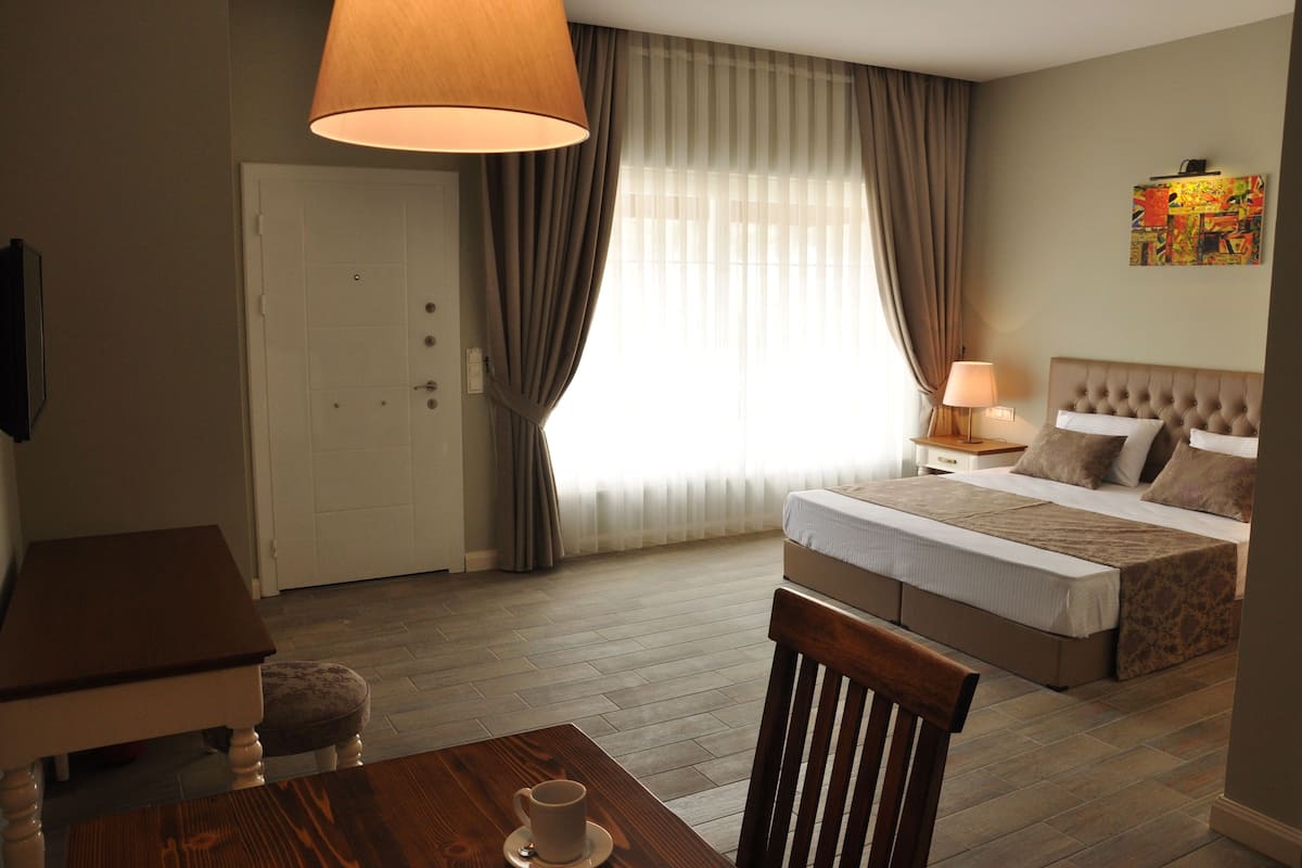 A hotel room with a bed, bedside table, lamp, chair, and a table with a cup.