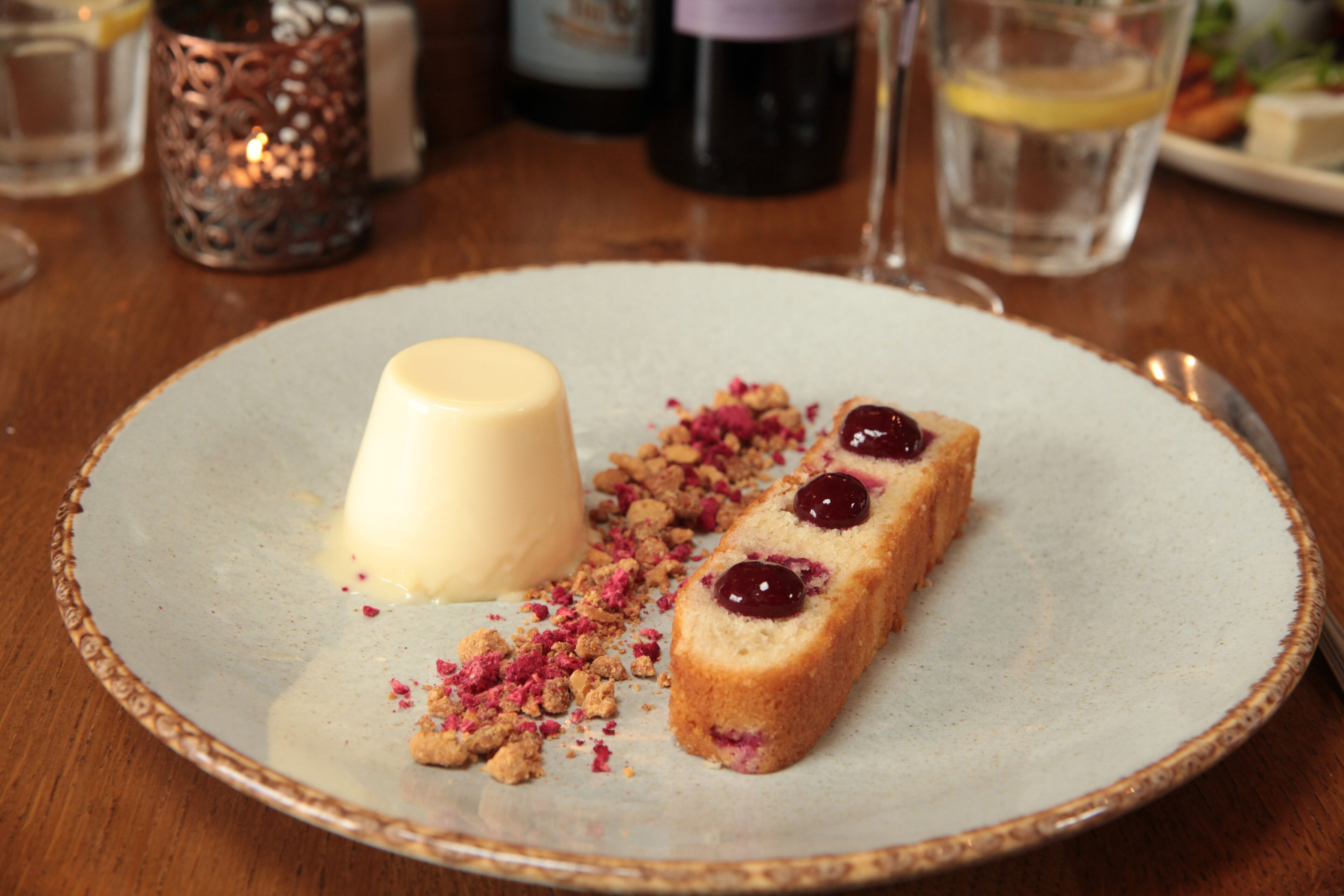 A dessert plate with a white dessert, a slice of cake with cherries, and crumbs on a ceramic plate.