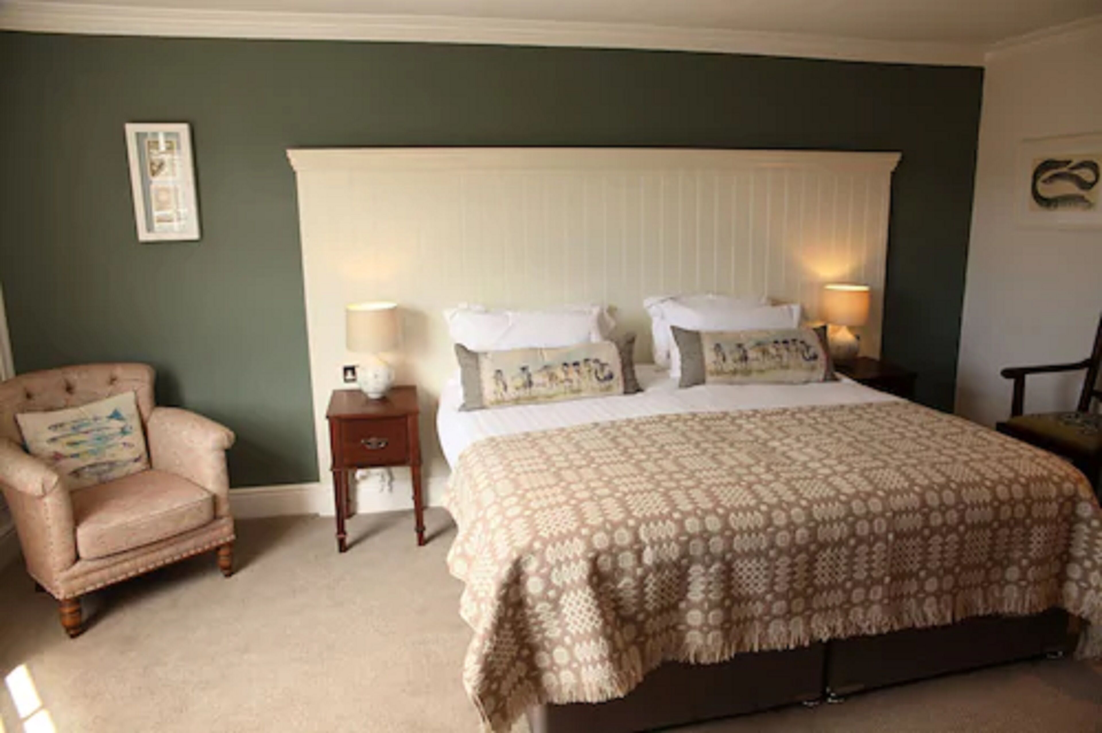 A bedroom with a large bed, a nightstand, a chair, and a wall-mounted picture.