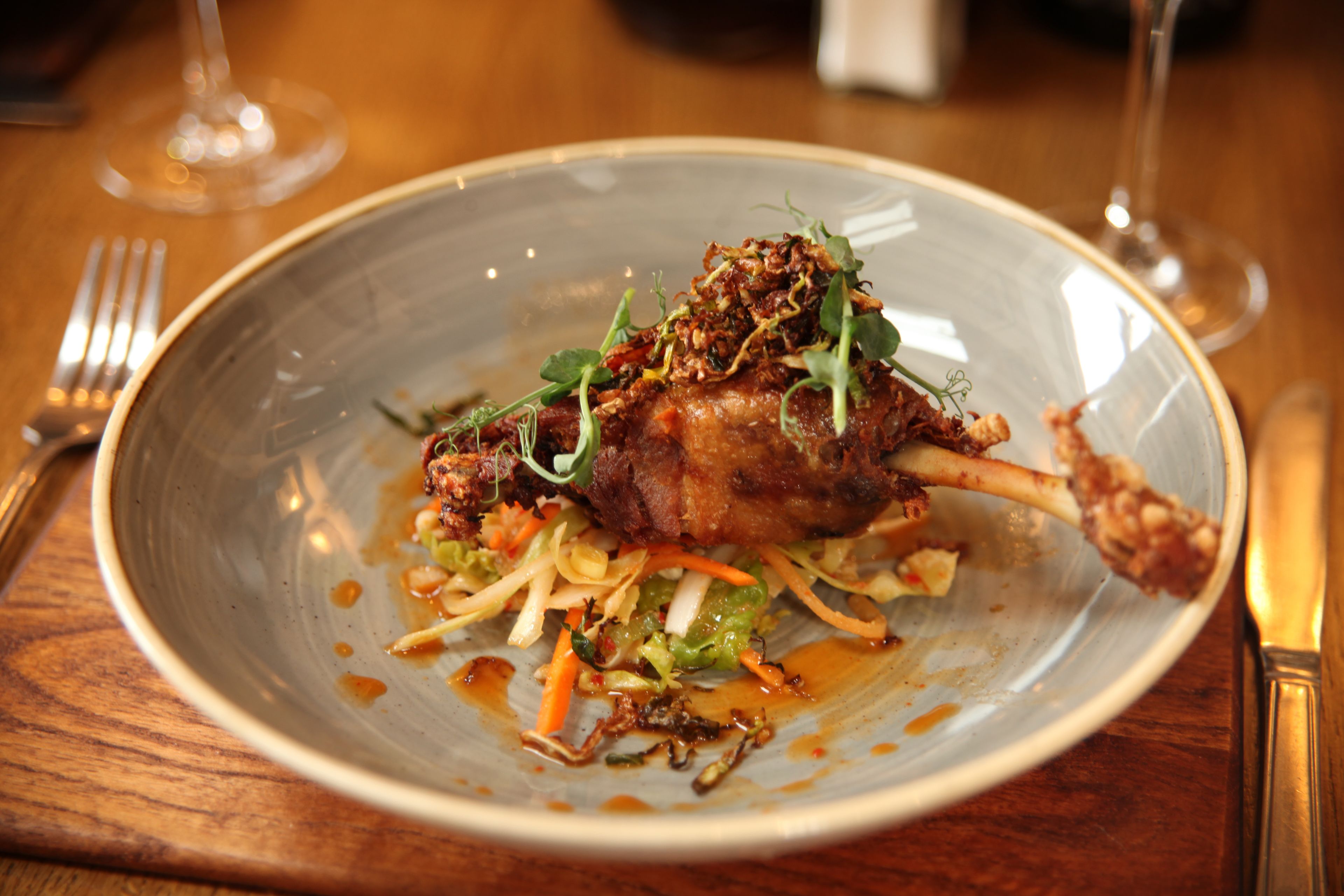 A plate of food with a lamb shank, vegetables, and sauce.