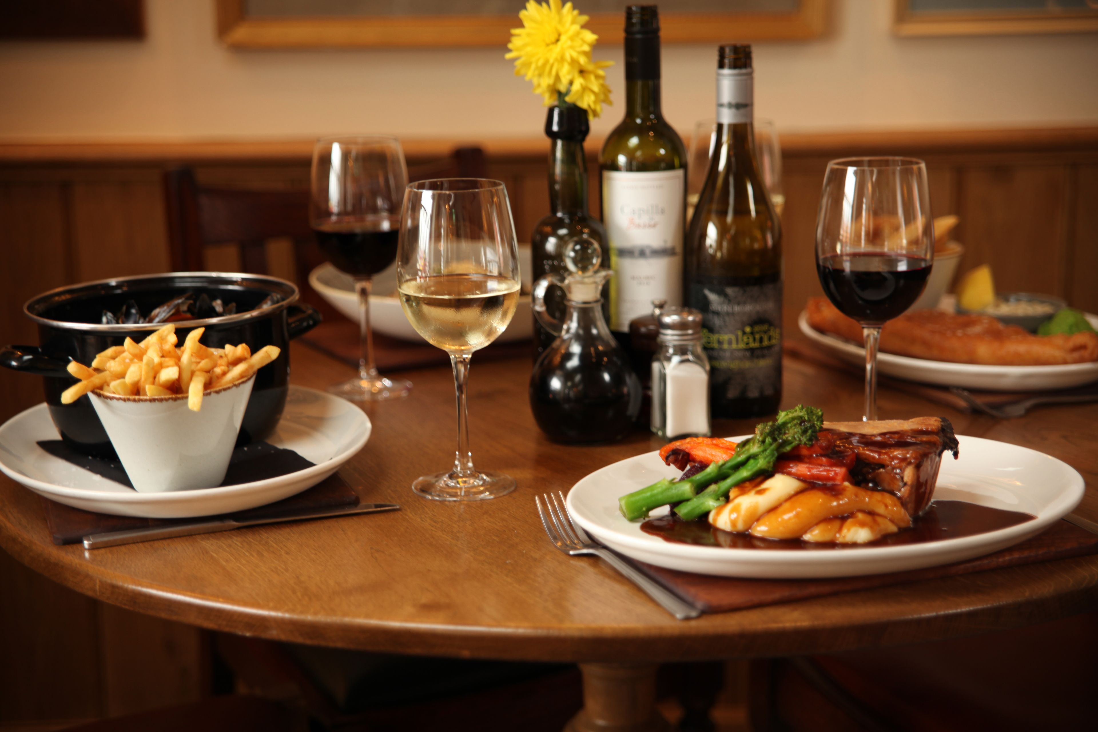 Una mesa de comedor con platos de comida, copas de vino y botellas.