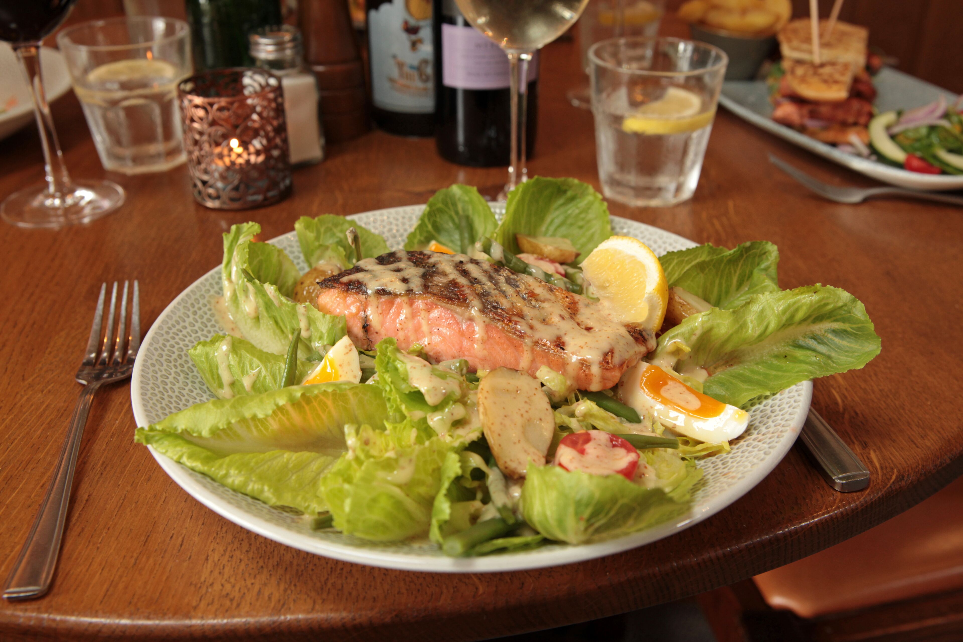 A plate of grilled salmon with salad and lemon on a wooden table.