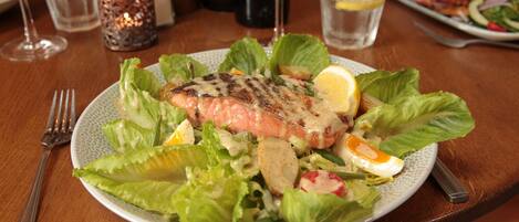 A plate of grilled salmon with salad and lemon on a wooden table.