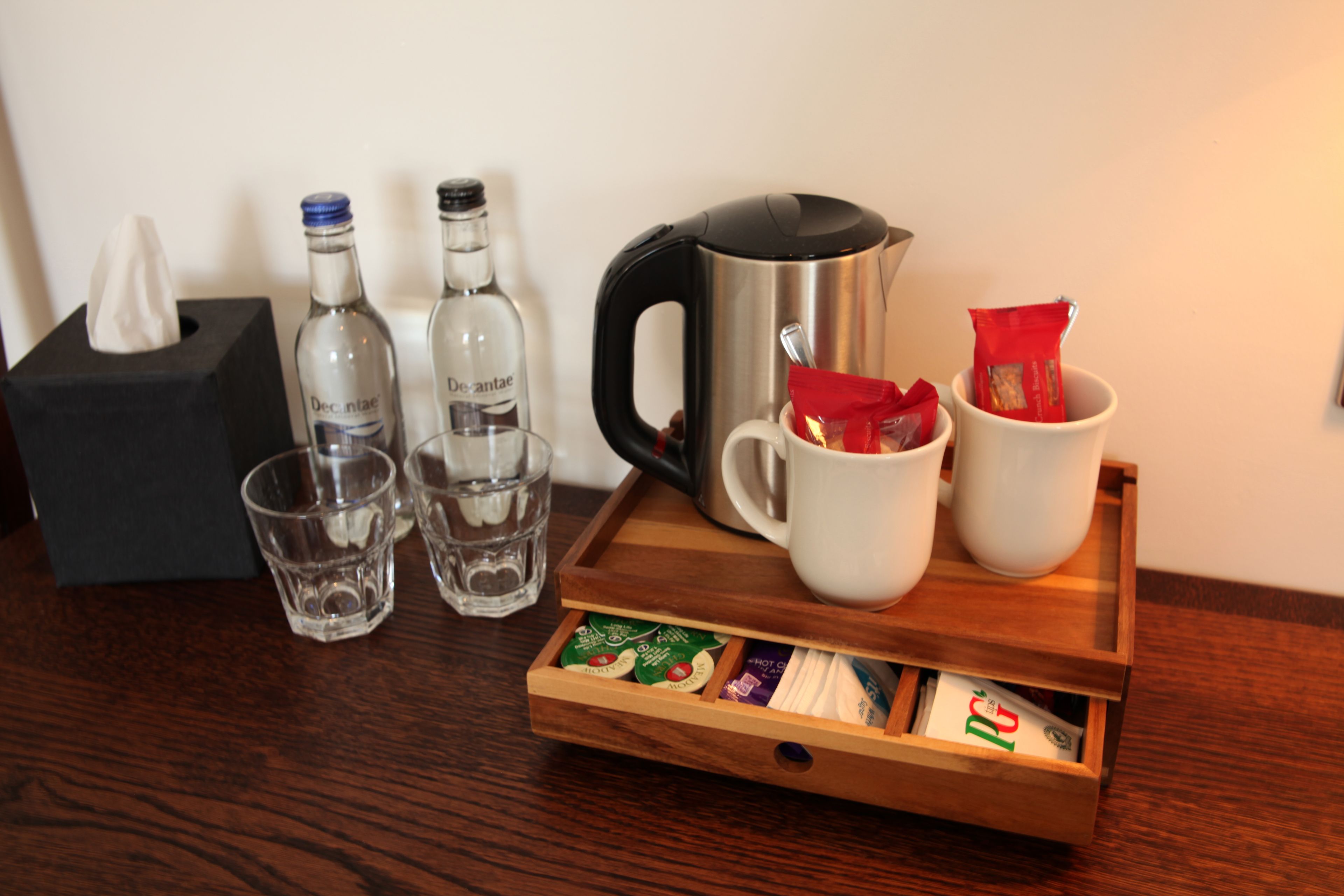 Una bandeja de madera con una cafetera, dos tazas, una caja de pañuelos y dos botellas de agua.
