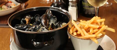 A dining table with a bowl of mussels, a cup of fries, and two glasses of wine.