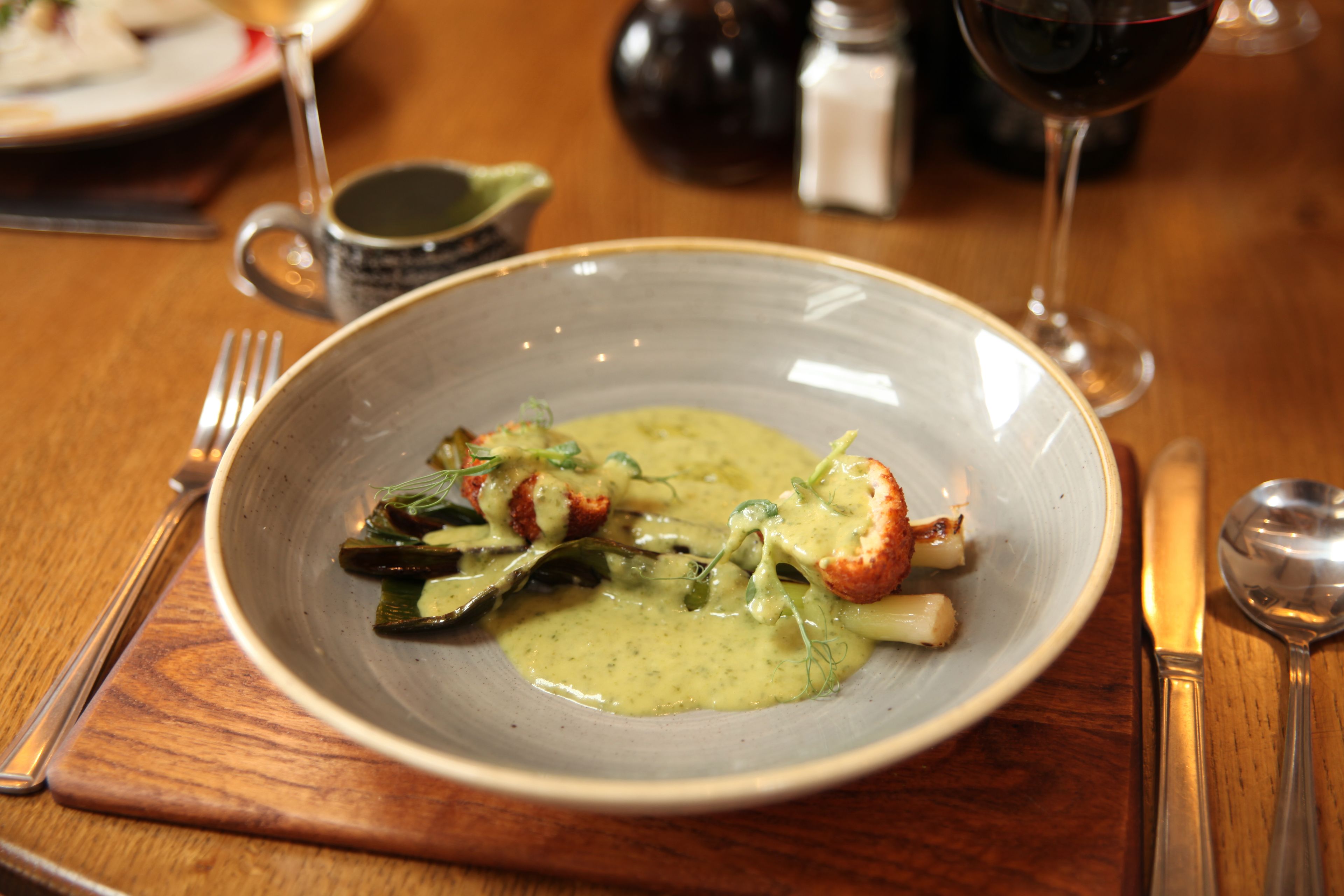 A plate of food with a green sauce, a fork, and a spoon on a wooden table.