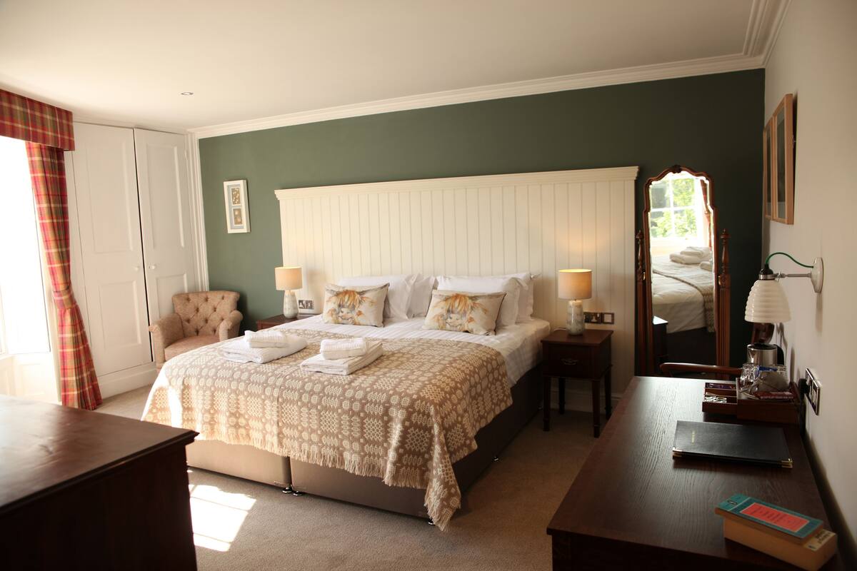 A neatly arranged bedroom with a large bed, bedside tables, a chair, and a desk.
