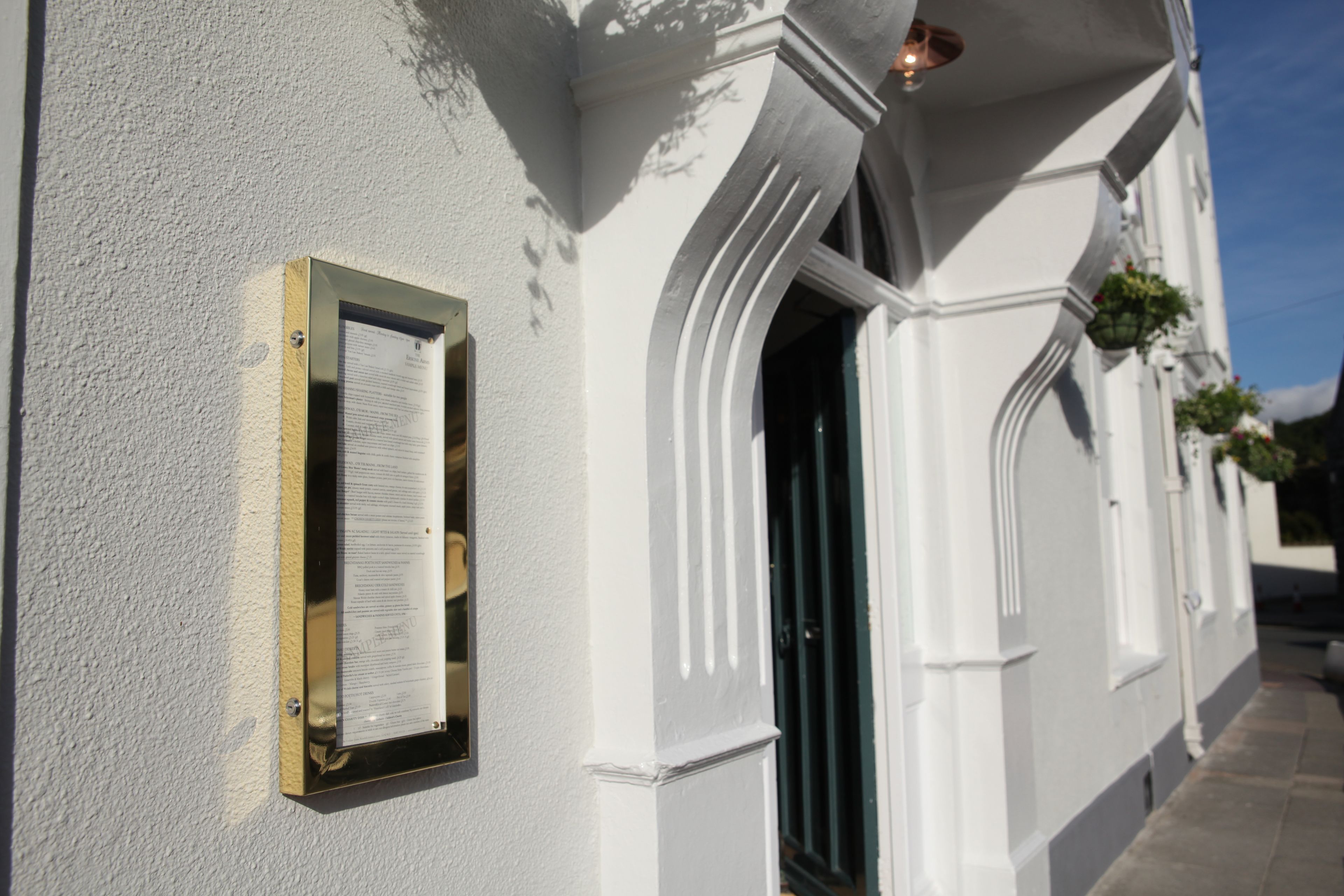 Un edificio con fachada blanca, un cartel en la pared y una puerta con marco negro.