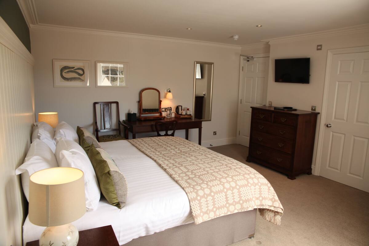A bedroom with a bed, bedside lamp, dresser, mirror, and a TV on the wall.