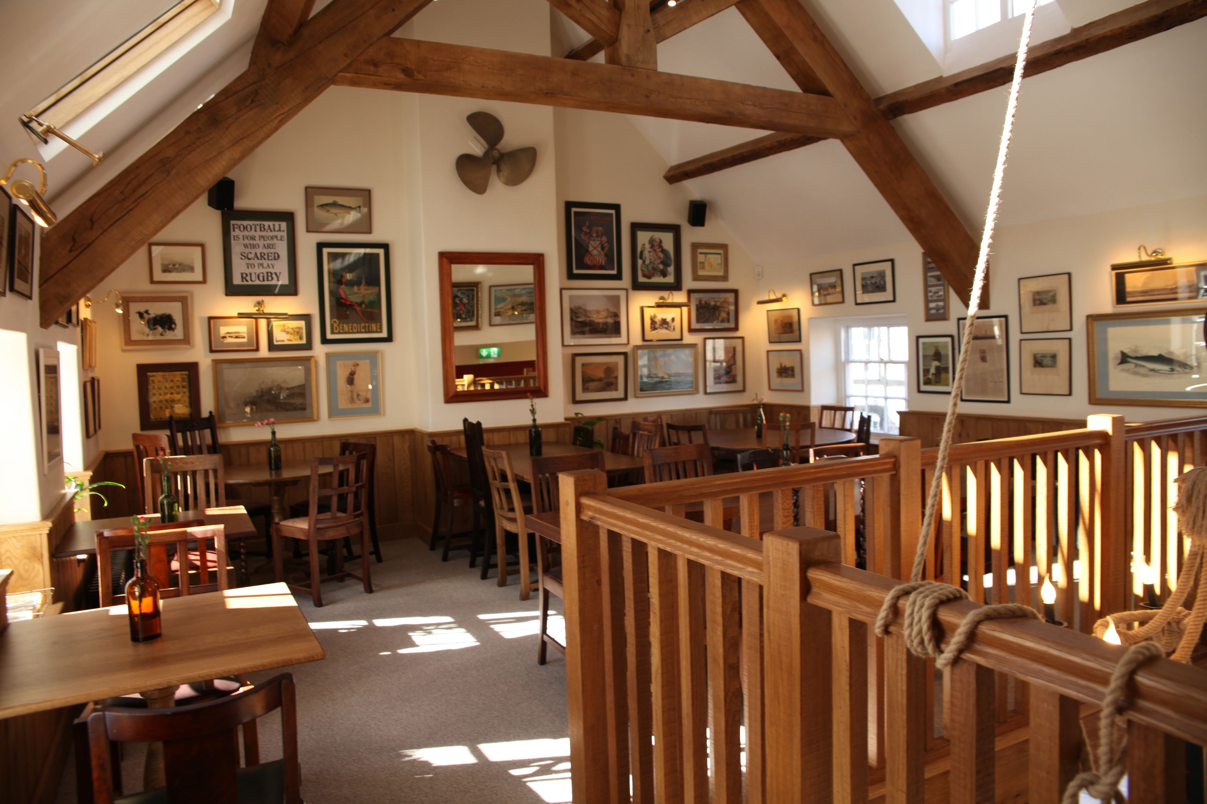 Un espace repas avec des meubles en bois, des tableaux encadrés aux murs et un plafond haut avec des poutres apparentes.