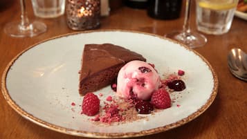 Een nagerechtenbord met chocoladecake en ijs, versierd met frambozen en een laagje cacaopoeder.