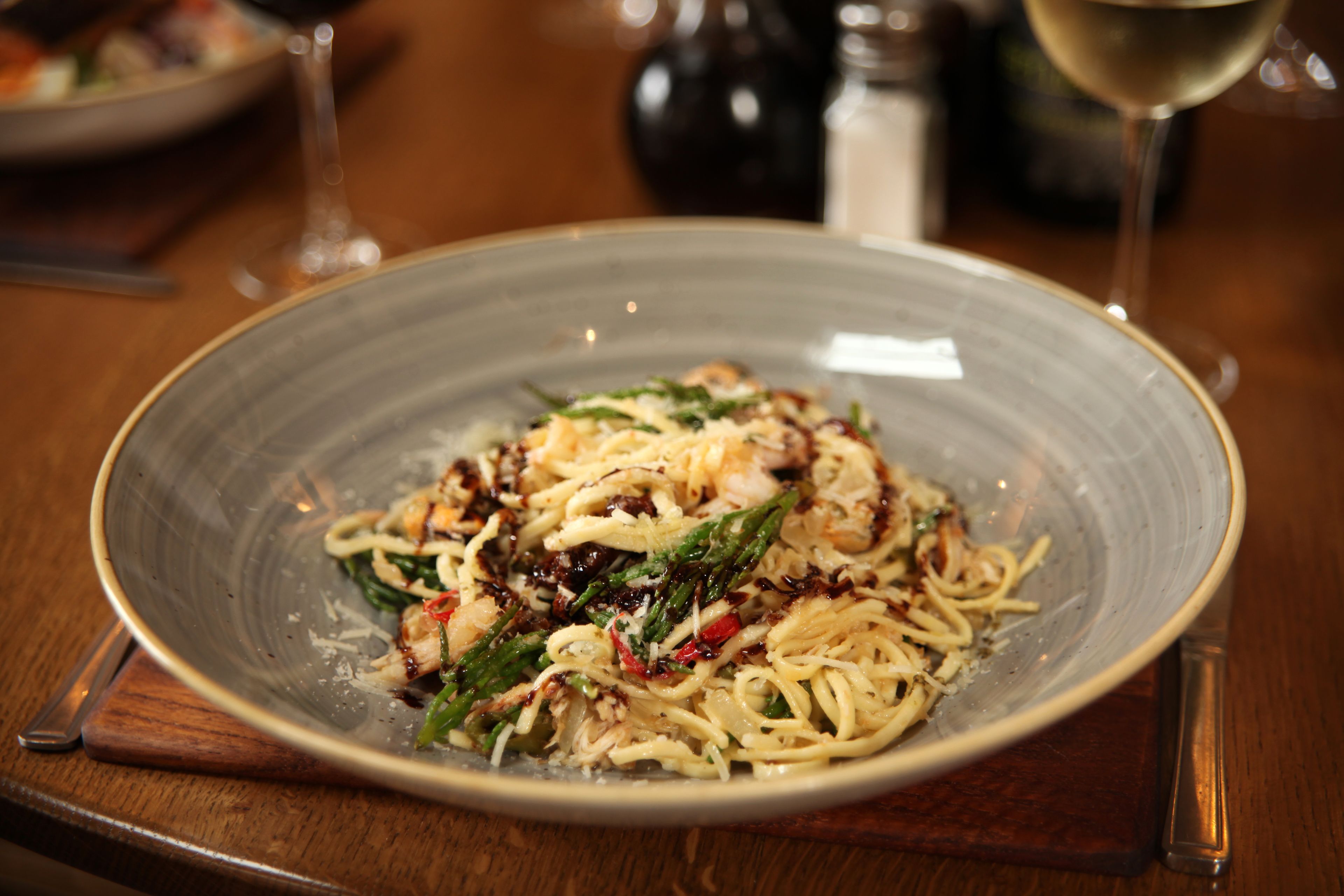 A plate of pasta with vegetables and cheese on a wooden table.