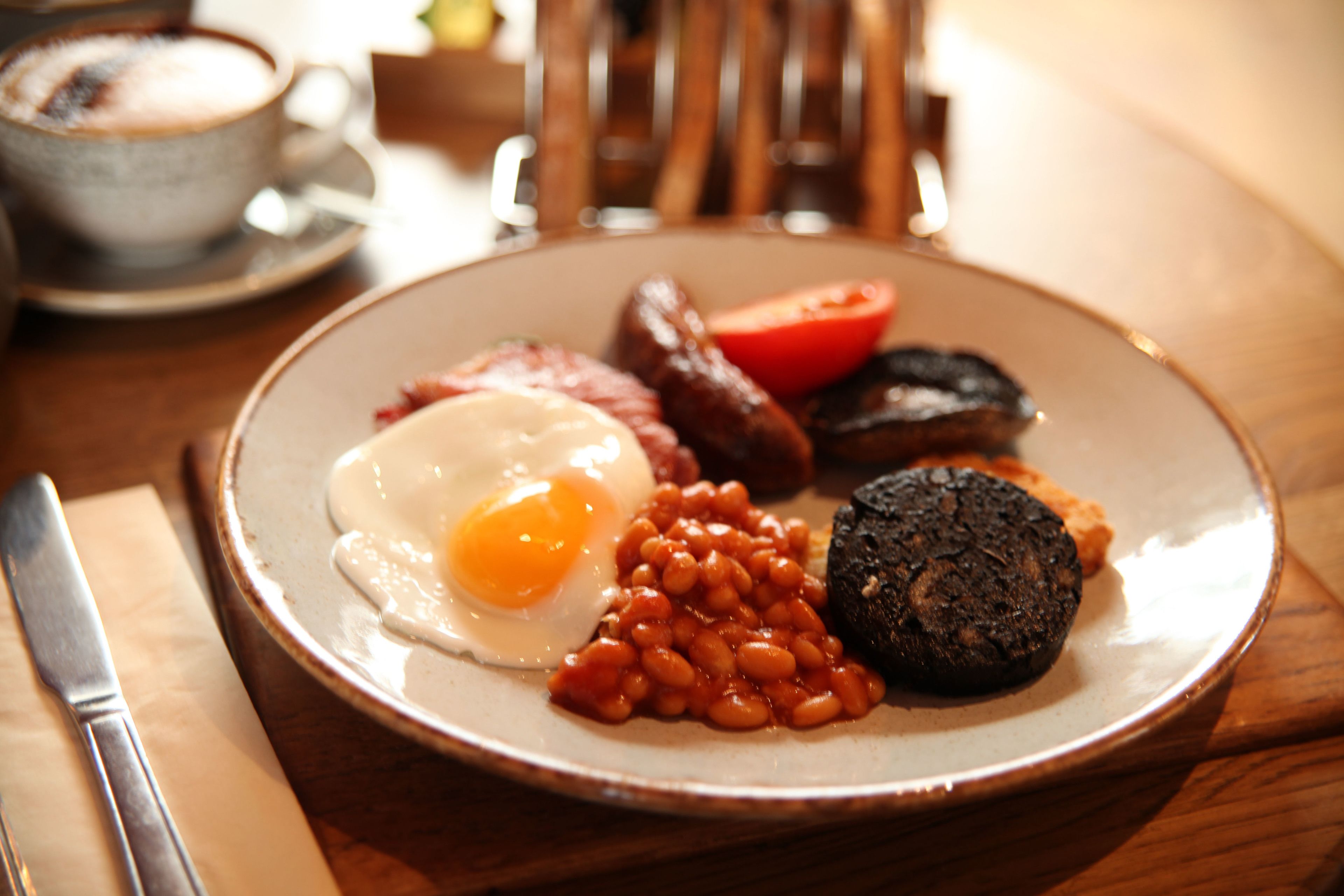 Une assiette de nourriture pour le petit-déjeuner comprenant des œufs, des haricots, des saucisses et une tranche de tomate.