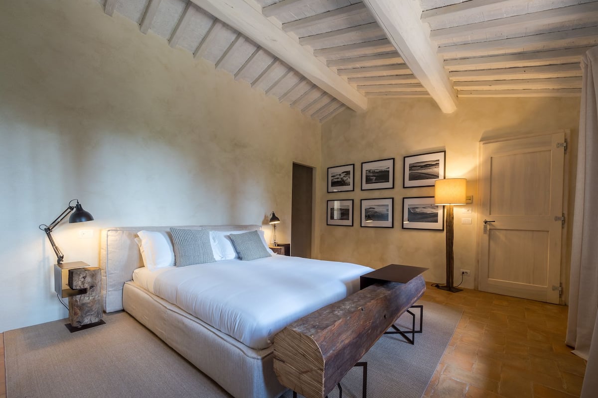 A bedroom with a large bed, bedside tables, a bench, and framed pictures on the wall.