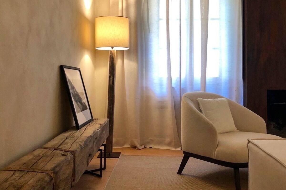 A cozy living room with a wooden bench, a white armchair, a floor lamp, and a framed picture on the wall.