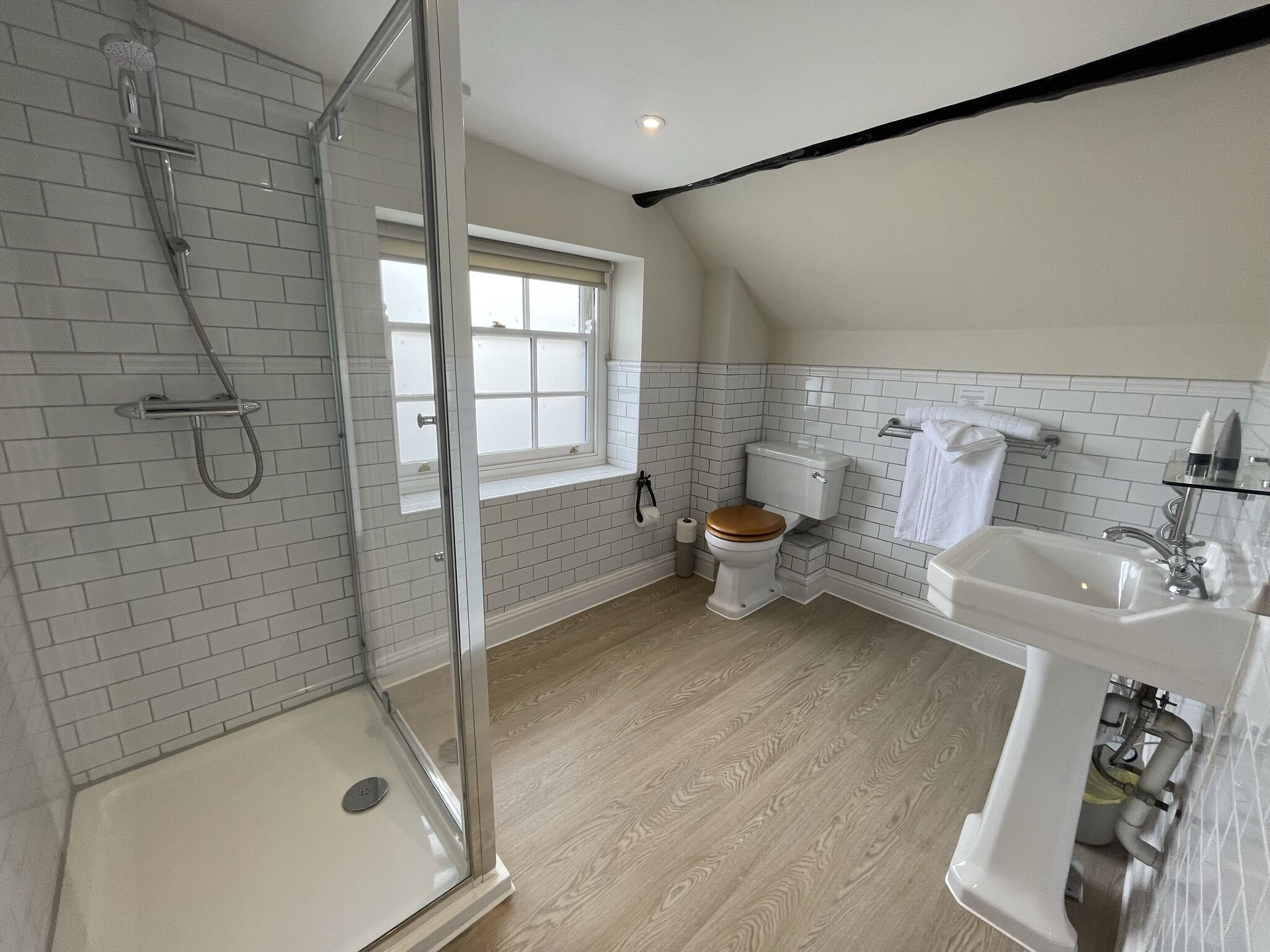 A modern bathroom with a glass shower enclosure, a toilet, a sink, and a window.