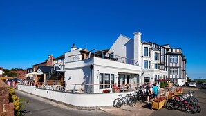 Un edificio frente al agua con balcón, bicicletas y mesas al aire libre.