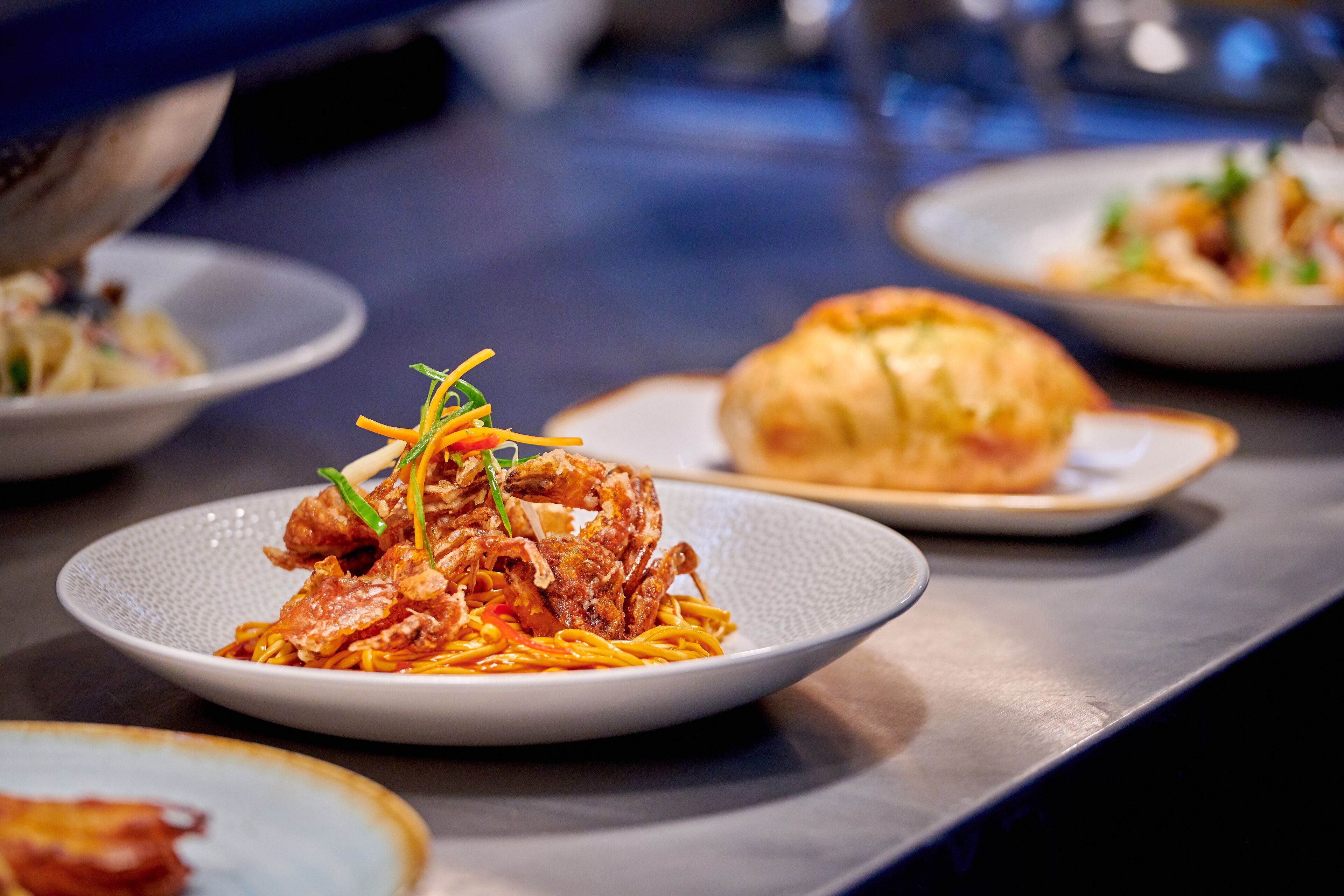 A dining table with various dishes, including noodles and a bread roll.