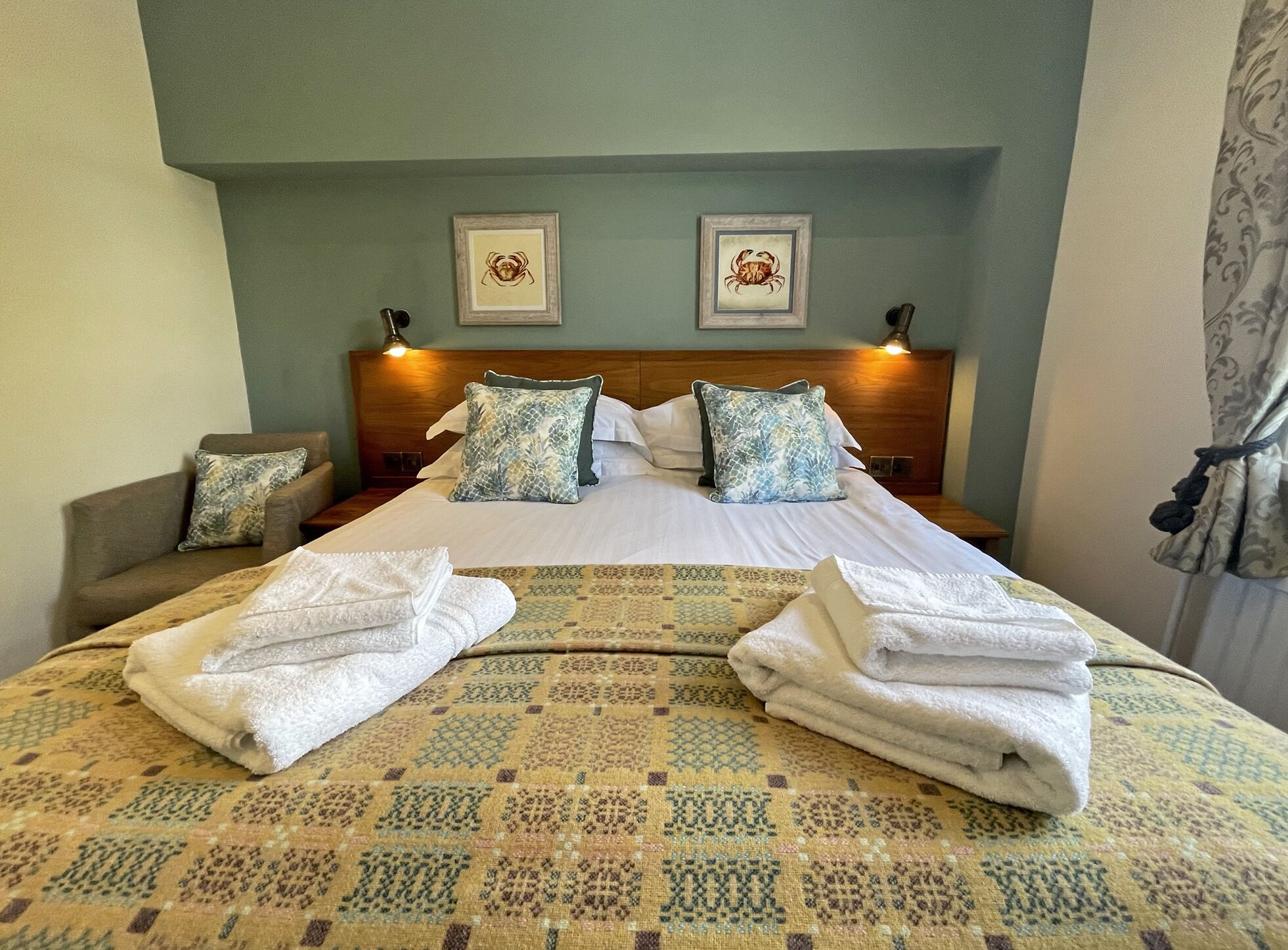 Una habitación de hotel con una cama bien hecha, dos cuadros en la pared y una mesita de noche con una lámpara.