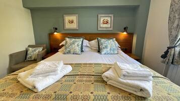 Una habitación de hotel con una cama bien hecha, dos cuadros en la pared y una mesita de noche con una lámpara.