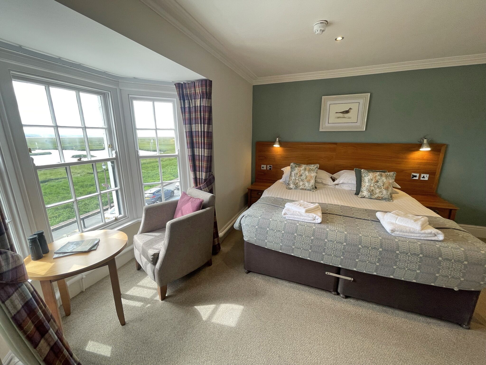 A hotel room with a large bed, a chair, a small table, and a window with a view of the outdoors.
