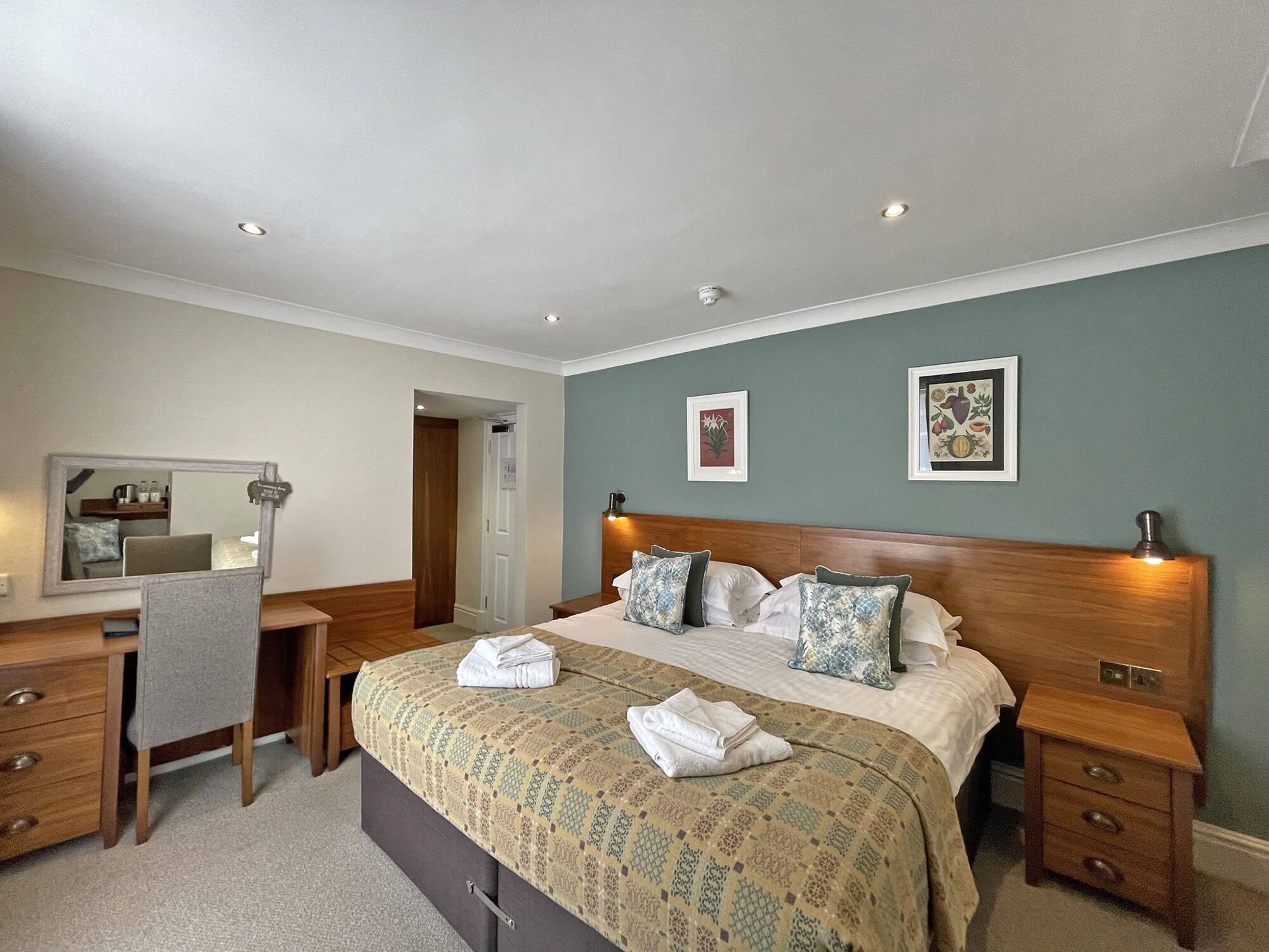A hotel room with a bed, bedside tables, a desk, a chair, and a mirror.
