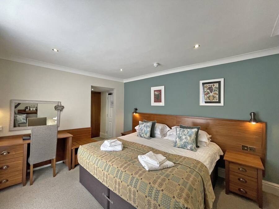 A hotel room with a bed, bedside tables, a desk, a chair, and a mirror.