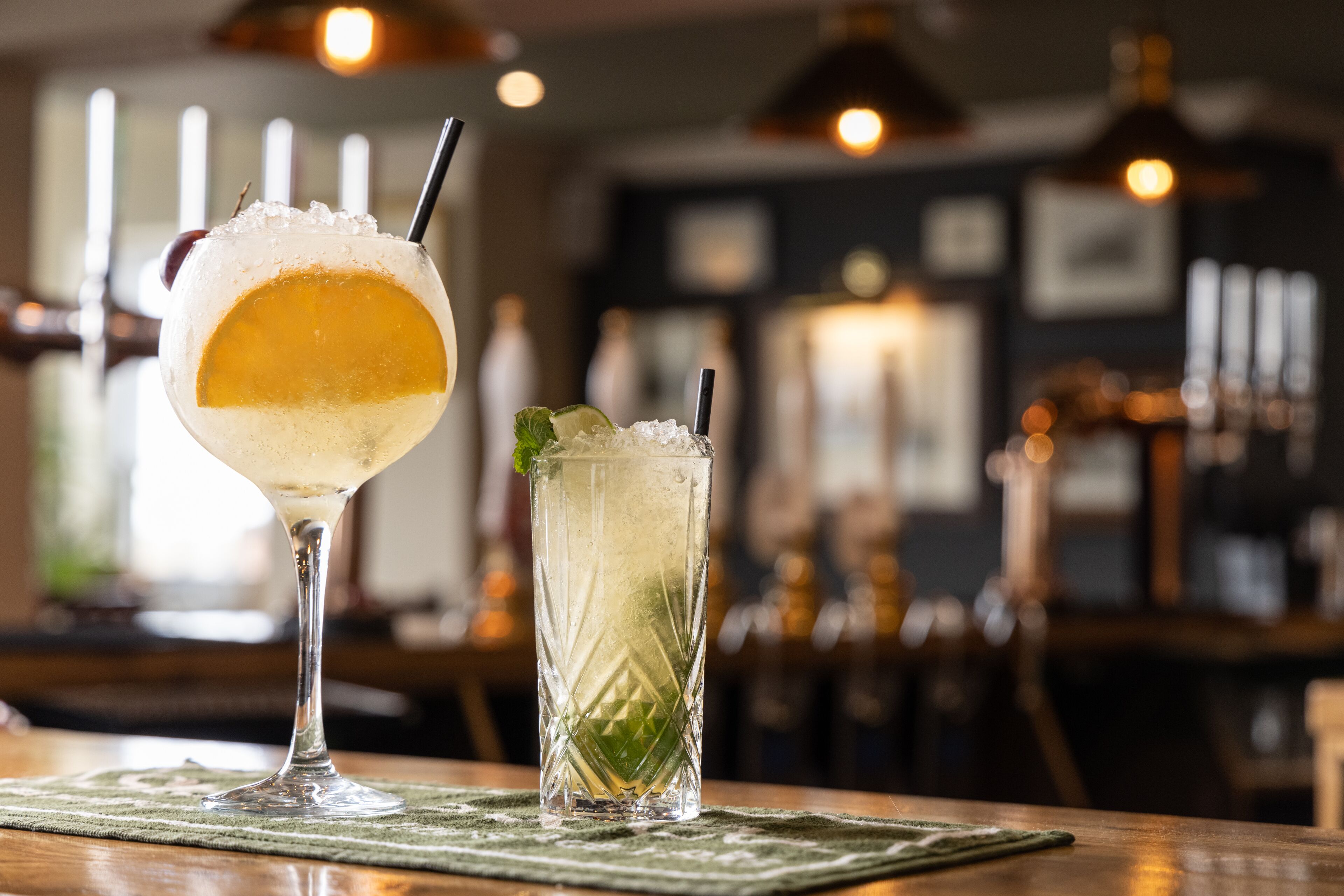 Two drinks on a bar mat in a dimly lit bar with a blurred background.