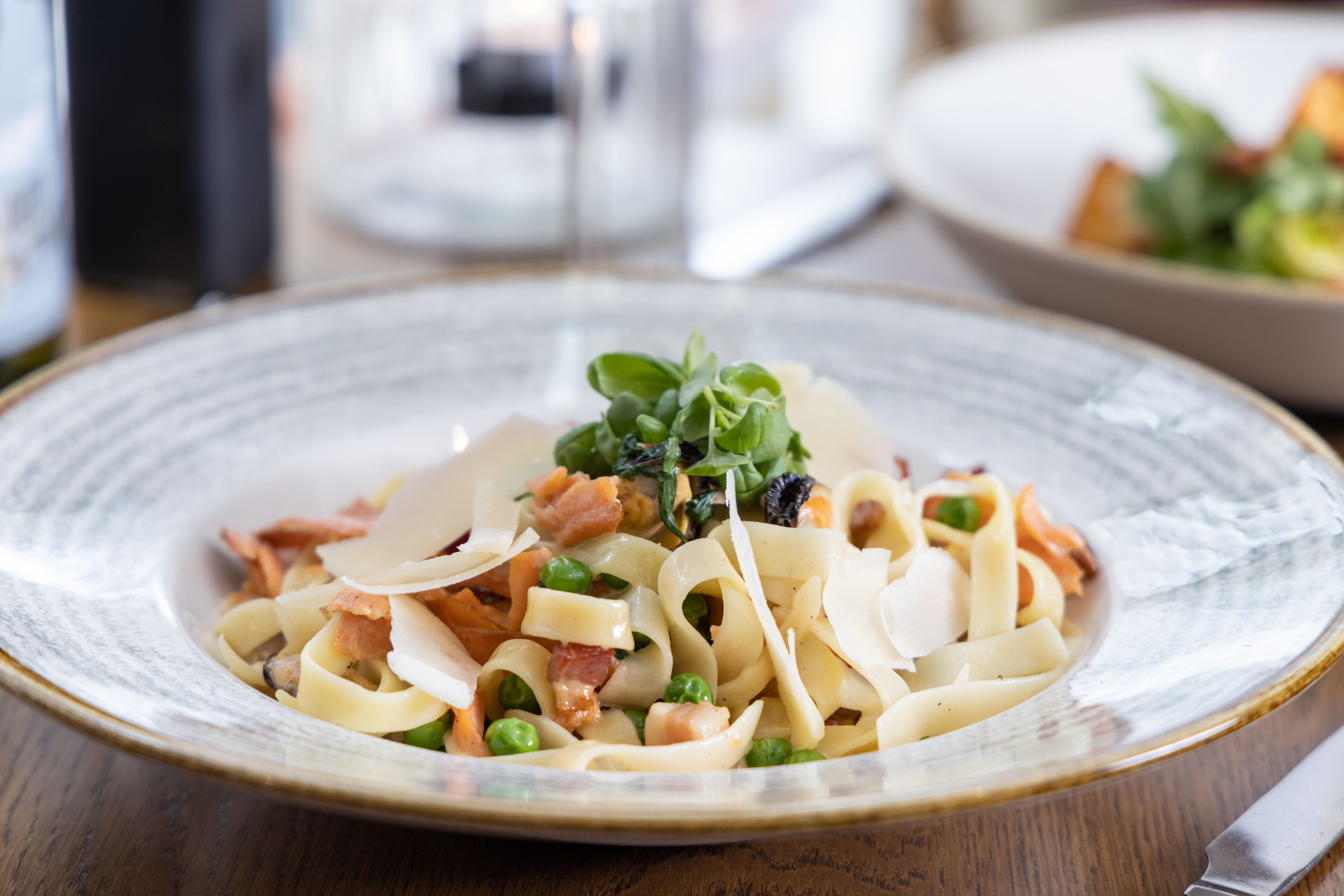 Un plato de pasta con guisantes, tocino y verduras de hoja.