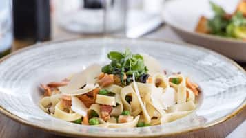 Un plato de pasta con guisantes, tocino y verduras de hoja.