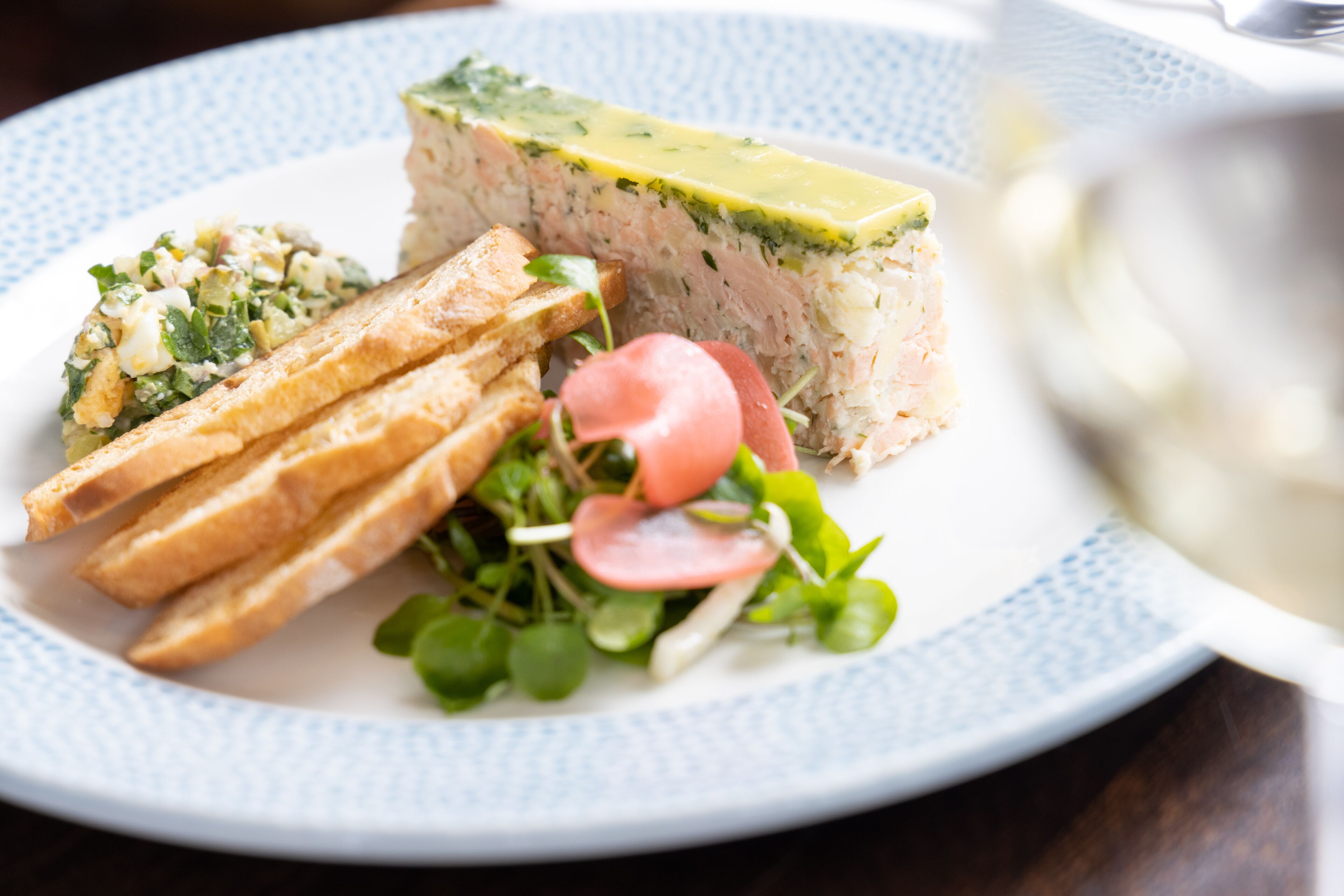 Un plato con tartar de pescado, pan tostado y una ensalada de rábanos y hojas verdes.