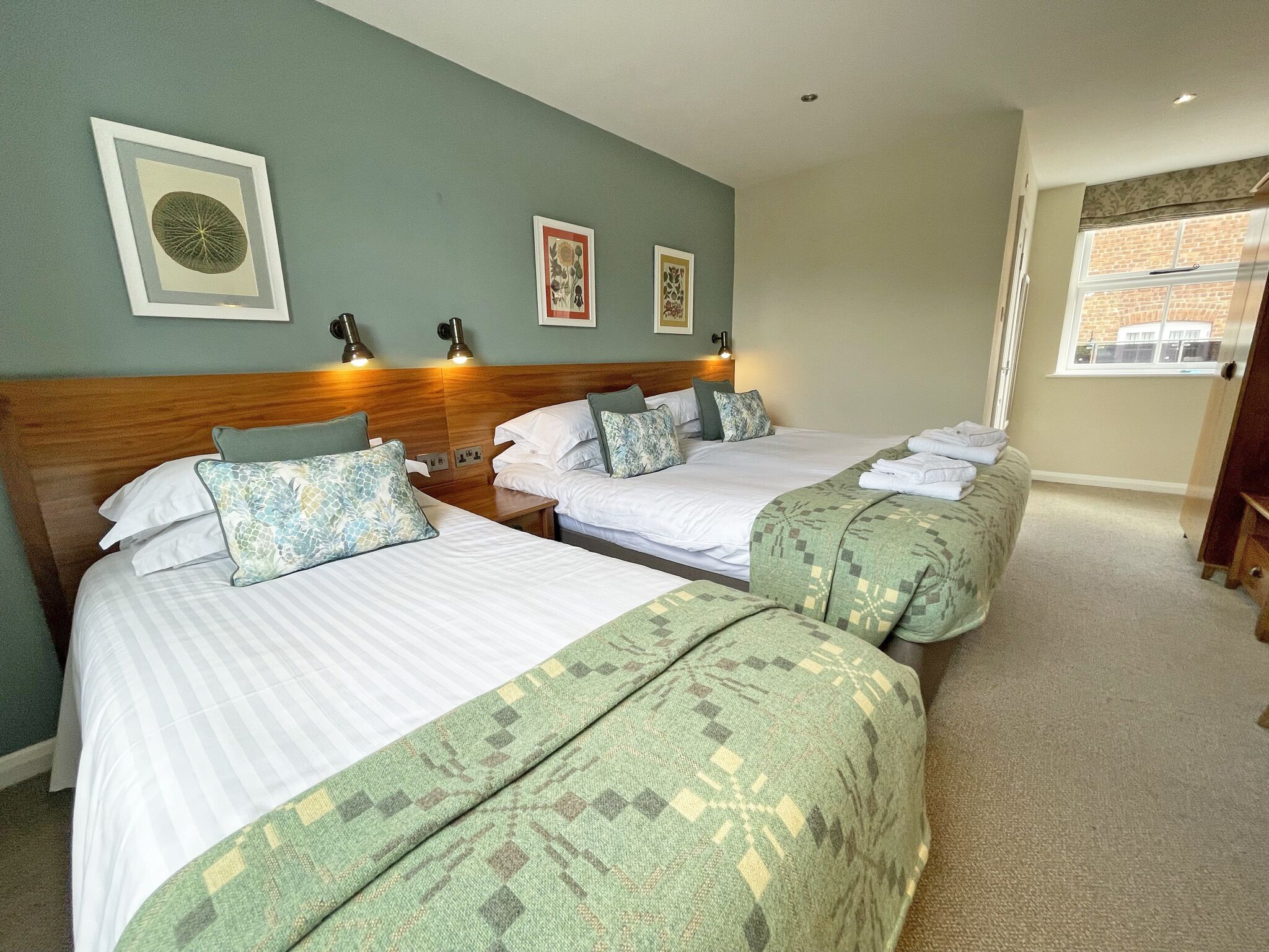 A hotel room with two beds, a wooden headboard, and a window with a view of a brick building.