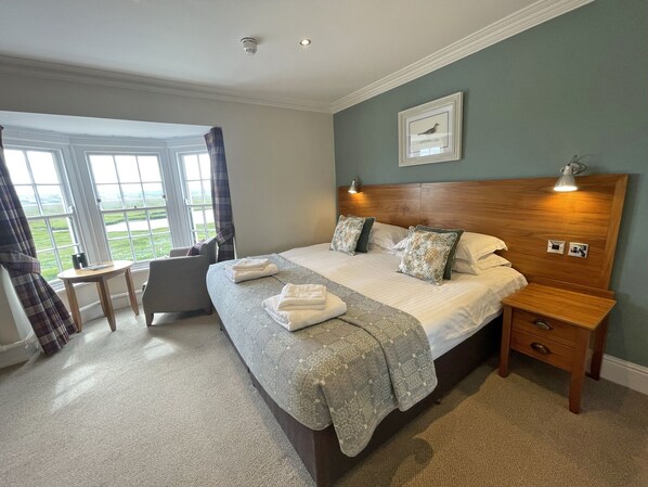 A neatly arranged bedroom with a large bed, bedside tables, a chair, and a window with curtains. - The Ship (Neston)