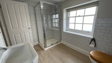 A bathroom with a glass-enclosed shower, a white bathtub, and a window with a view.