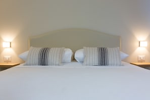 A neatly made bed with white linens and striped pillows, flanked by two bedside tables with wall-mounted lamps. - Mondello Martini (Palermo)