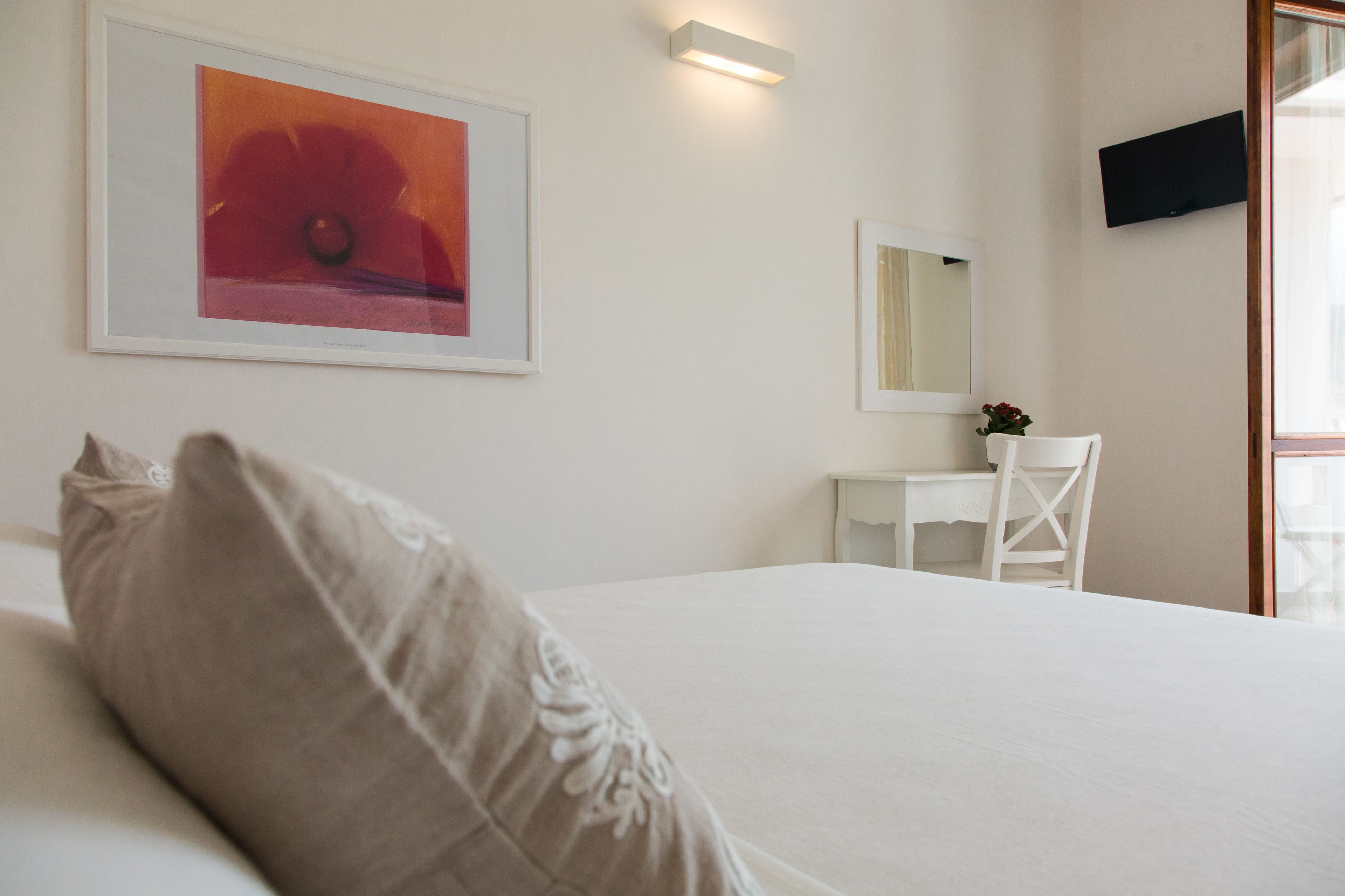 Hotellihuone, jossa on sänky, työpöytä, tuoli, peili ja seinällä oleva kehystetty taideteos.