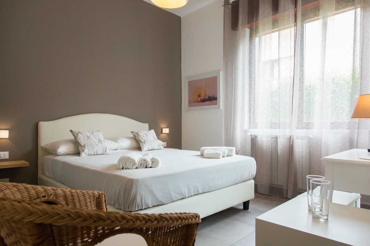 A neatly arranged bedroom with a large bed, bedside tables, a chair, and a window with curtains.