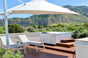 A rooftop terrace with white lounge chairs, a wooden deck, and a large white umbrella providing shade.