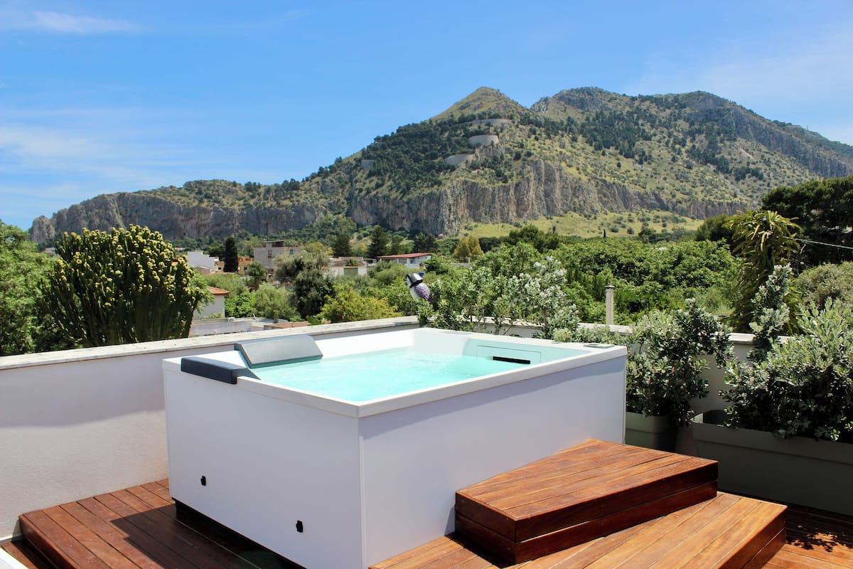 A rooftop swimming pool with a wooden deck and a view of a mountainous landscape.