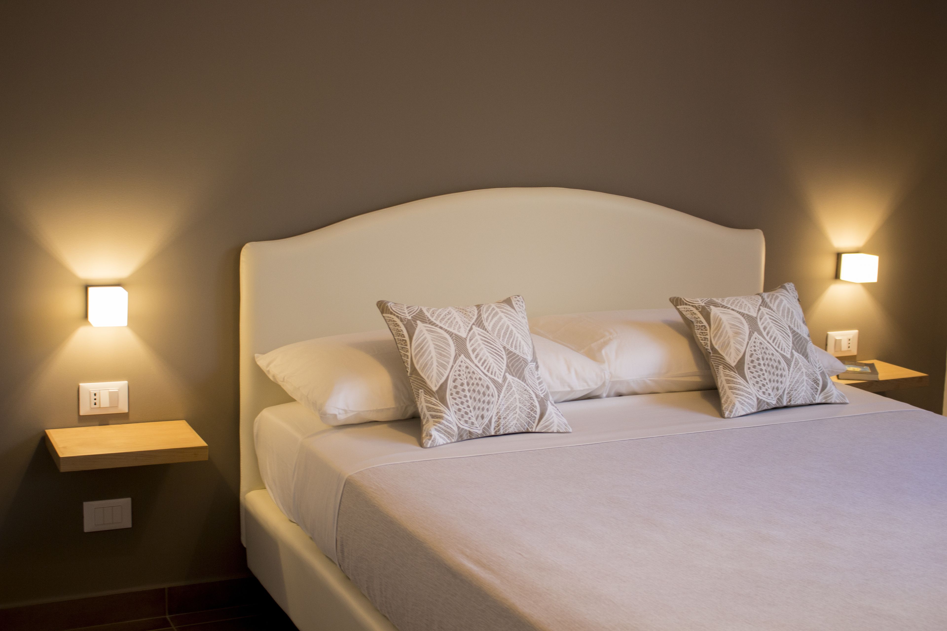 A neatly made bed with a white headboard and two bedside tables with wall-mounted lamps.