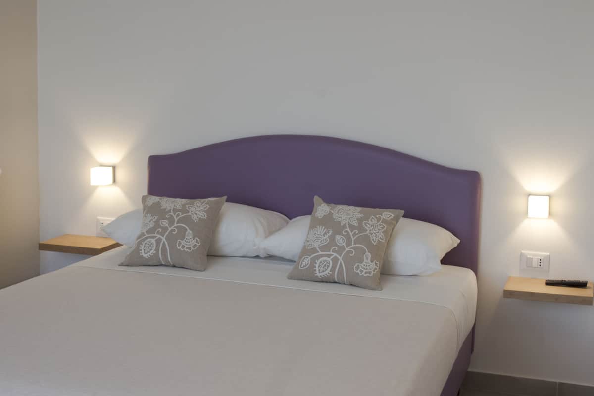 A neatly made bed with a purple headboard, two bedside tables with lamps, and floral-patterned pillows.
