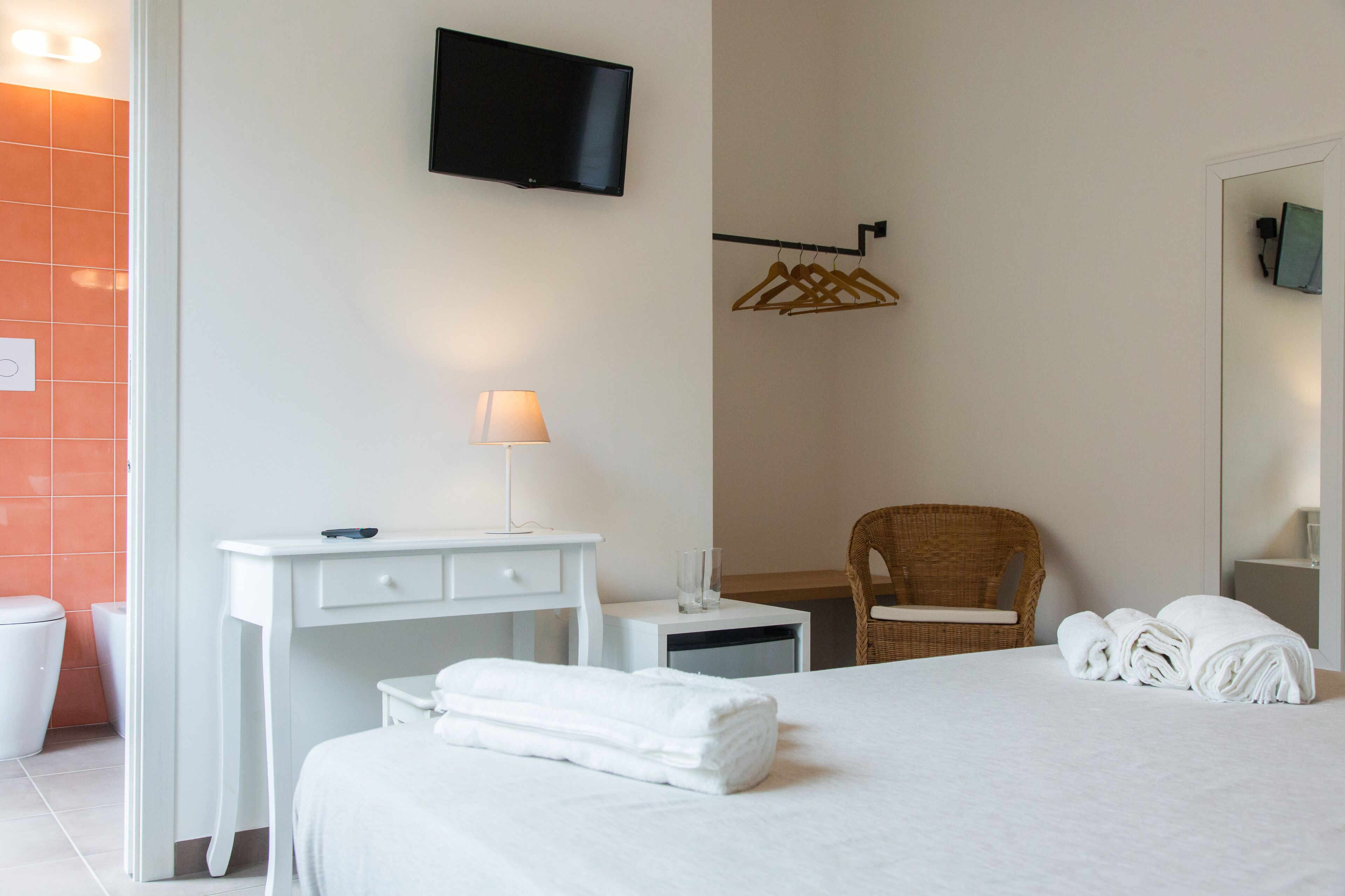 A hotel room with a bed, a desk, a chair, a TV, a lamp, a mirror, and a towel rack.