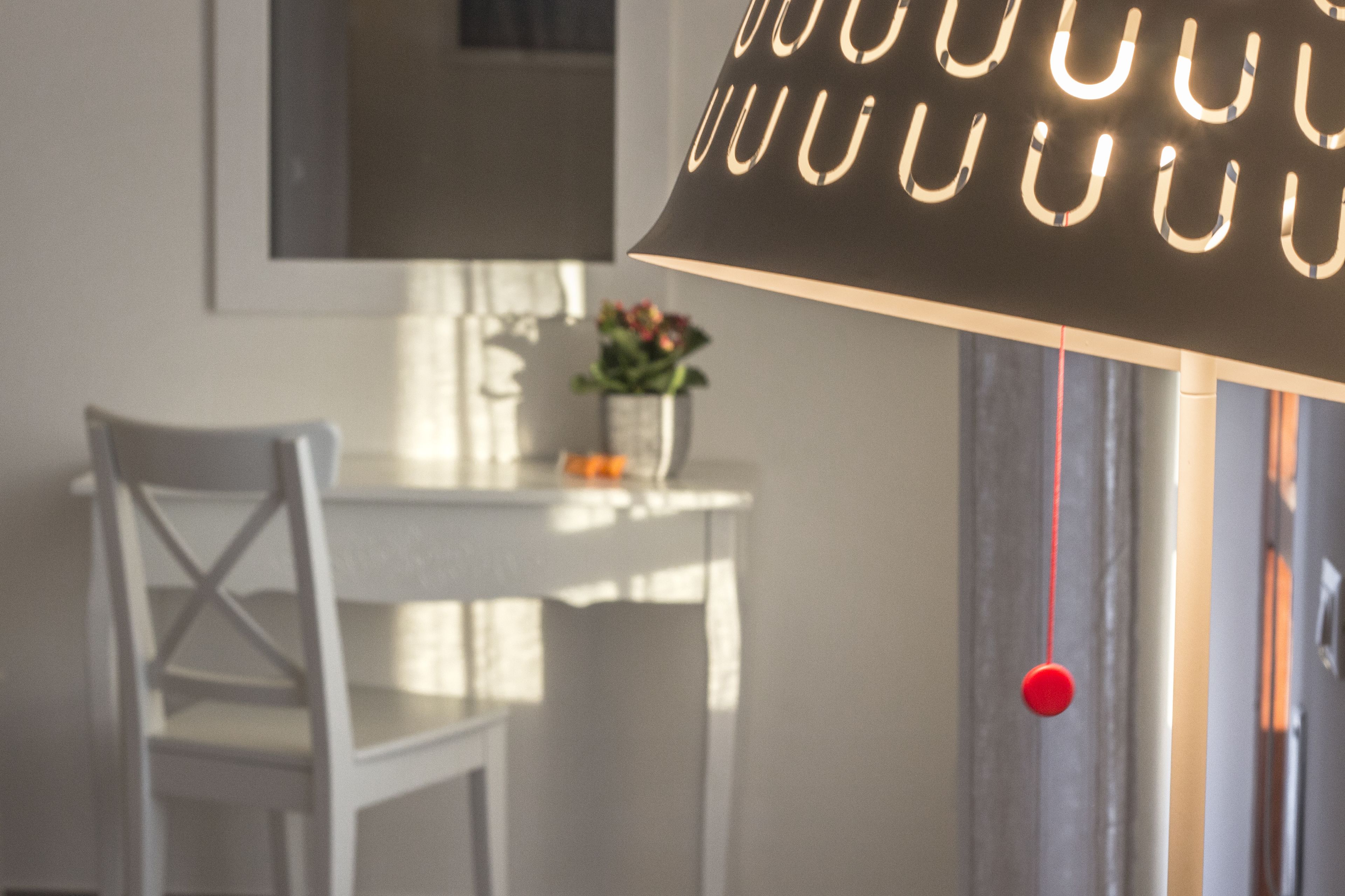 Een eethoek met een tafel, stoelen, een hanglamp en een rood voorwerp.