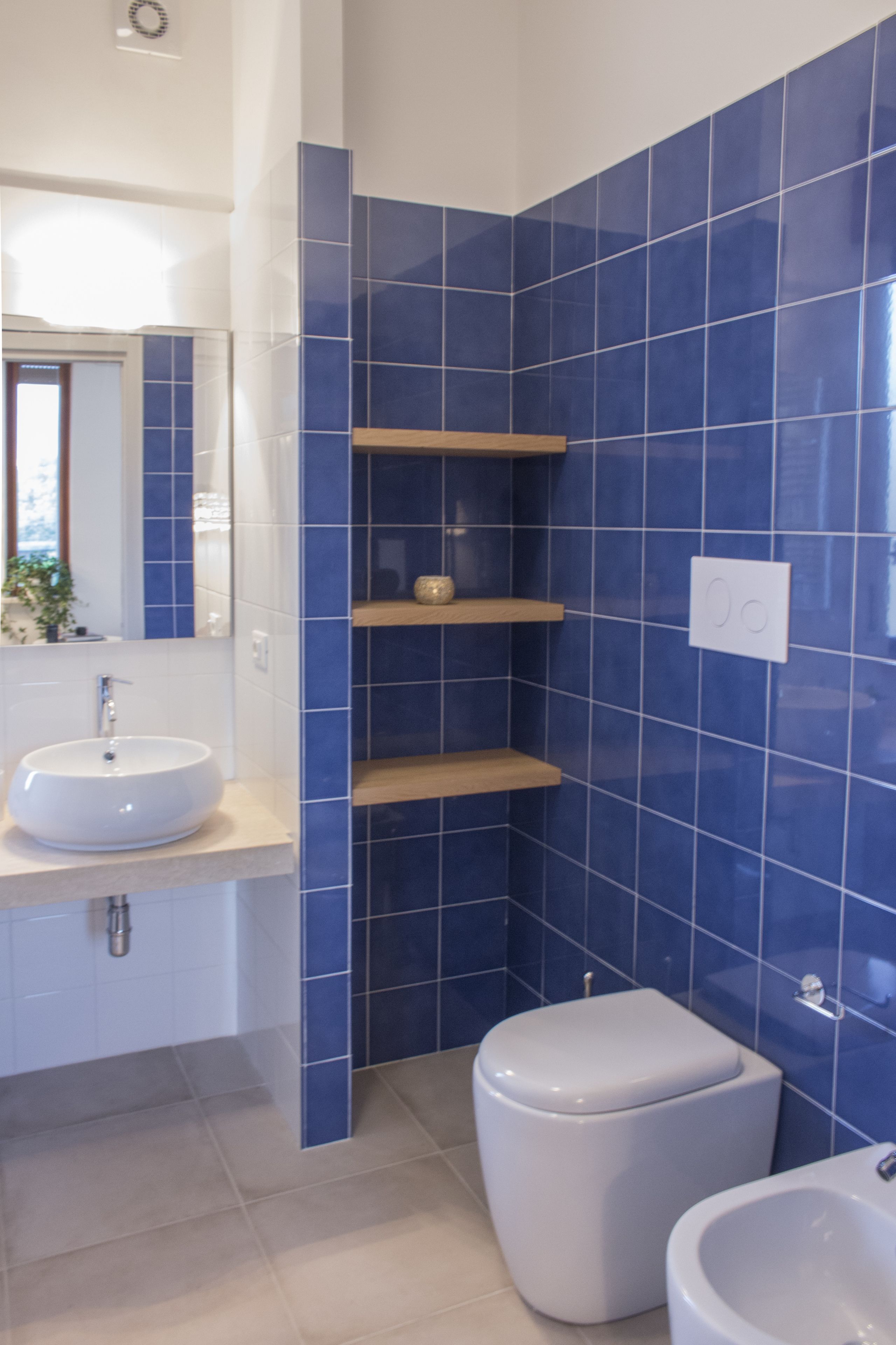 A bathroom with a white sink, a toilet, and a bidet. There are blue tiles on the walls and a mirror above the sink.