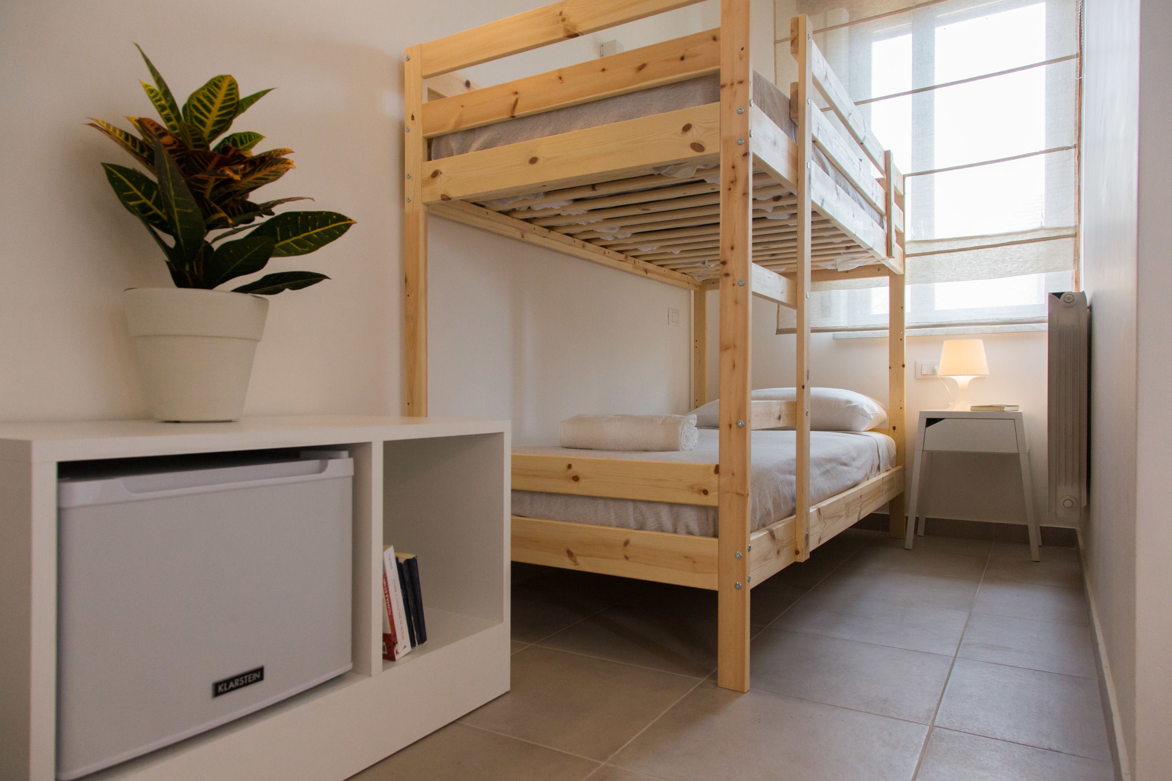Une chambre avec un lit superposé, un bureau blanc, une plante en pot et un petit réfrigérateur.
