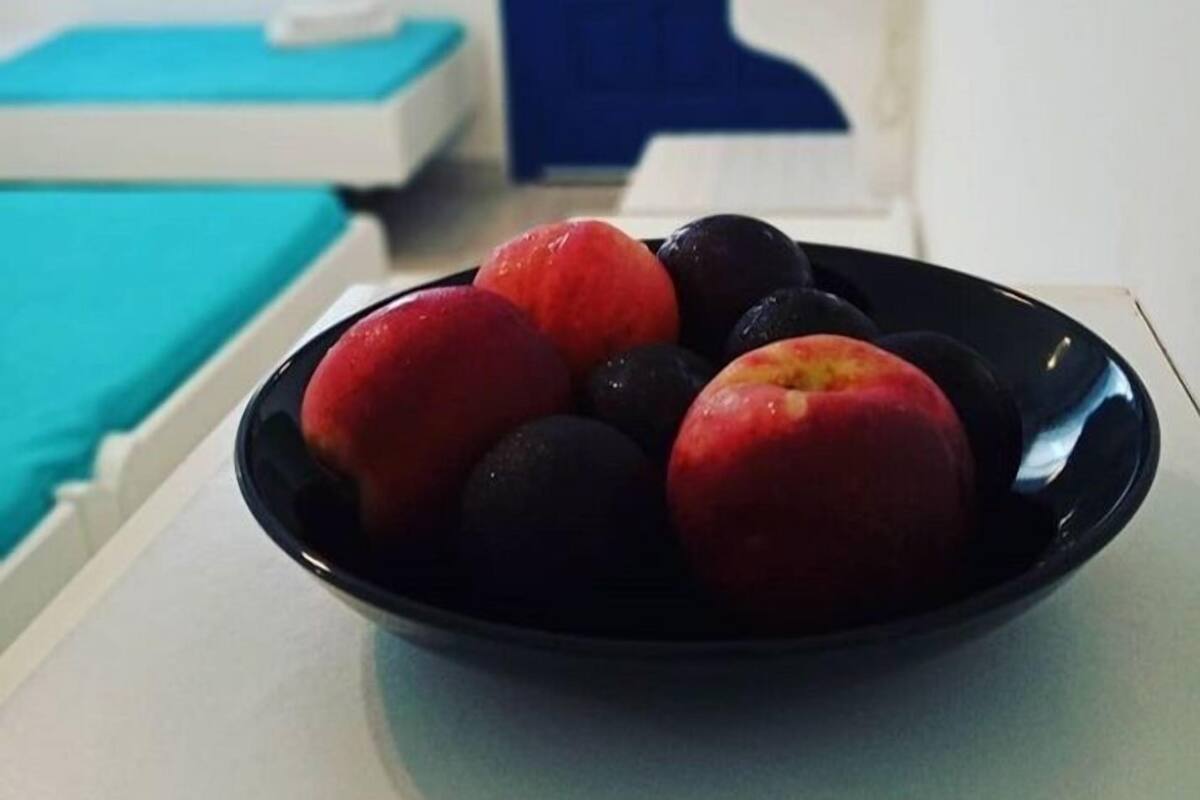 A room with a bed, a blue door, and a bowl of fruit on a table.